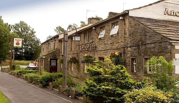 Stone building with a sign for Anchor Inn, surrounded by greenery and a pathway in a rural setting.
