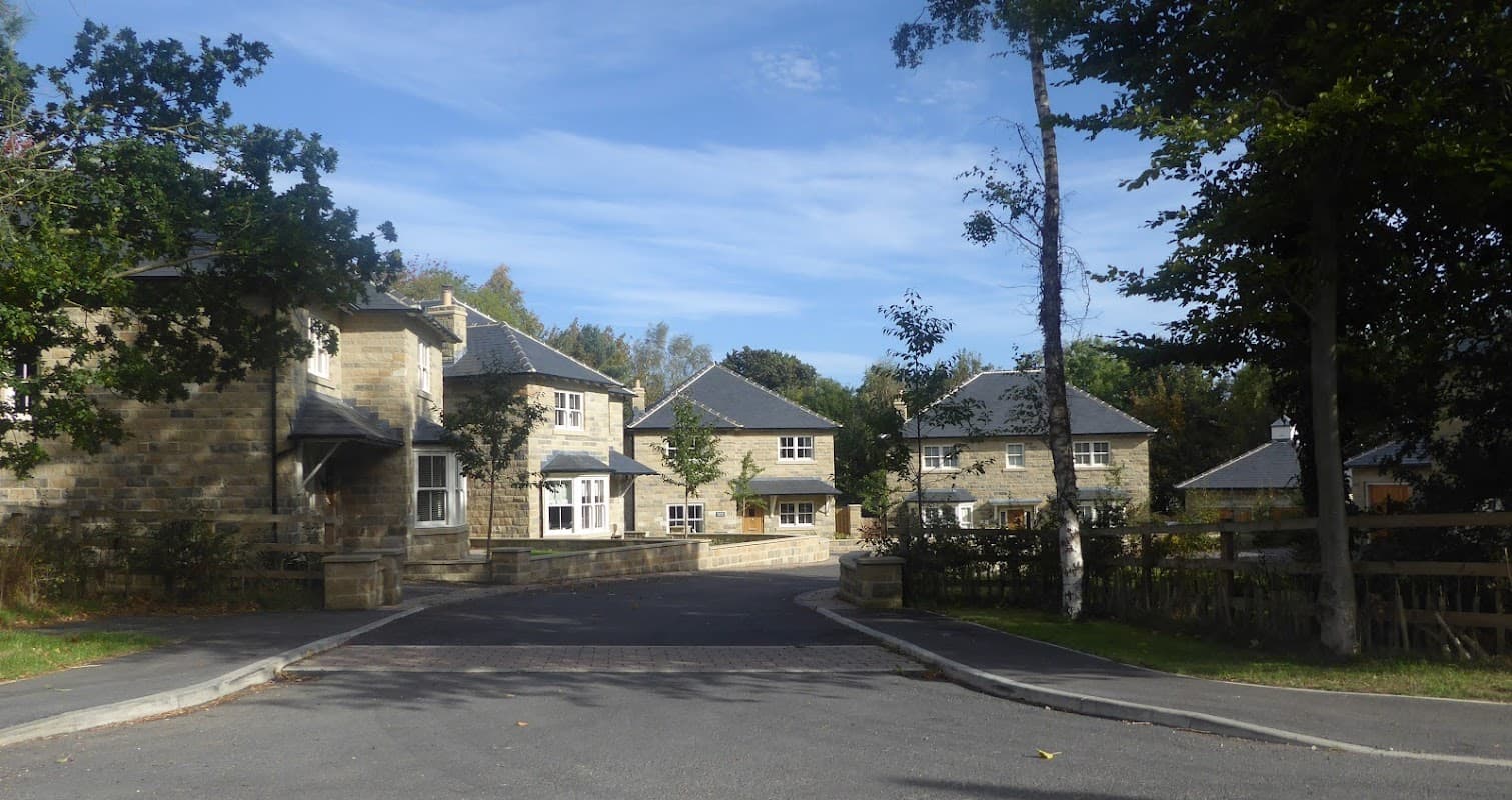 Stone buildings with slate roofs, surrounded by trees and a winding road in a rural setting.