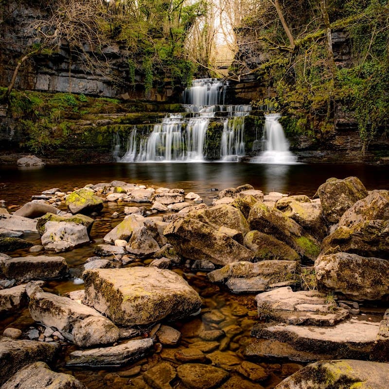 Serene waterfall cascading over rocks, surrounded by lush greenery in Cotterdale, Yorkshire.