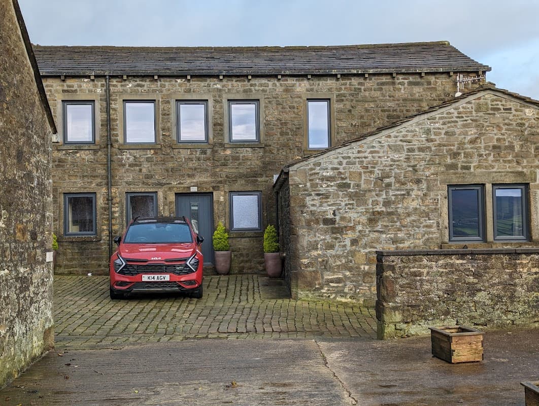 Stone cottages with a red car parked in front, surrounded by greenery and a cobblestone driveway.
