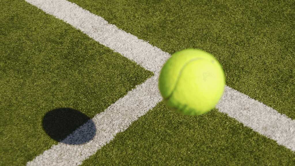 A bright yellow tennis ball bouncing near a white line on a green court surface.
