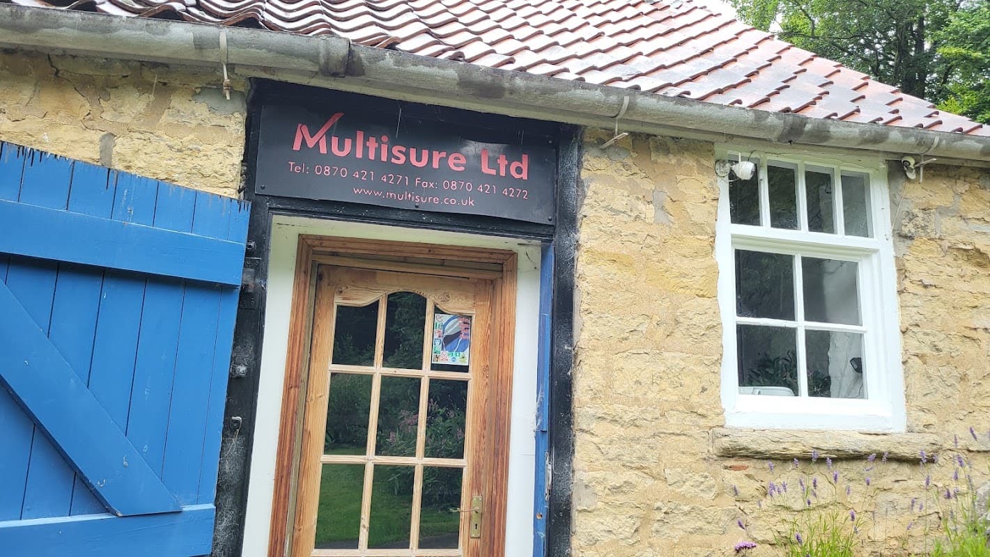 Shopfront of Multisure Ltd, featuring a blue door, stone wall, and a sign with contact details and website.