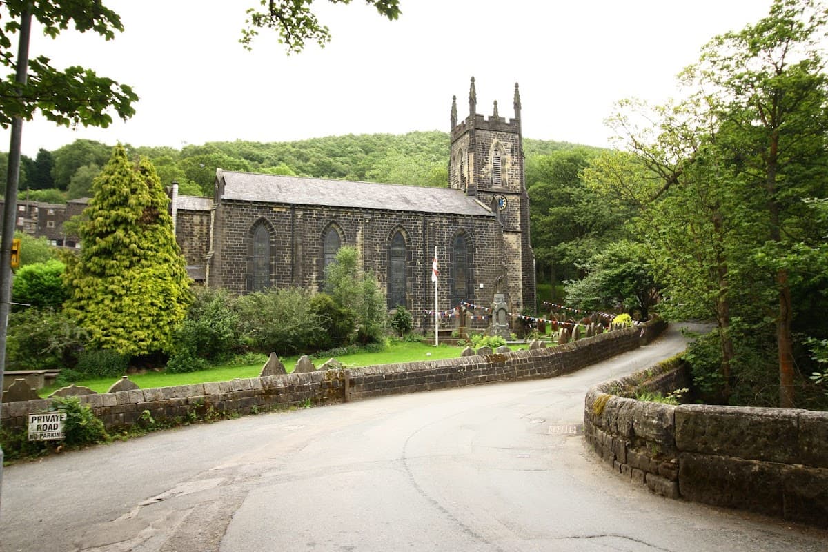 Historic stone church with a tall spire, surrounded by greenery and a winding road in Cragg Vale, Yorkshire.