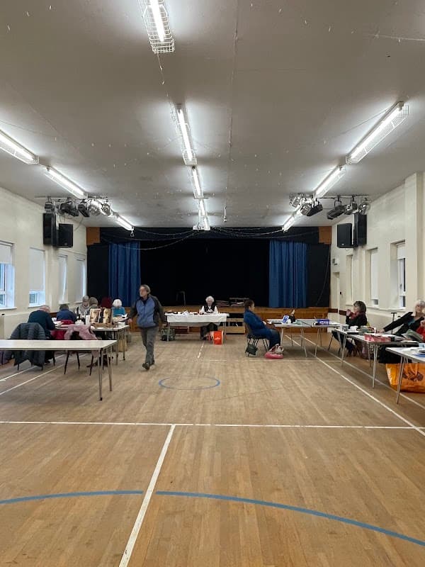 Spacious village hall interior with tables, chairs, and a stage in the background, set up for an event.