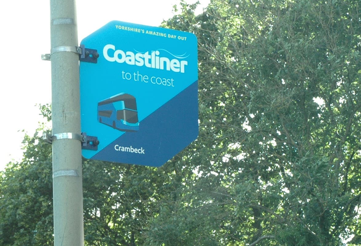 Coastliner bus stop sign in Crambeck, Yorkshire, with trees in the background.