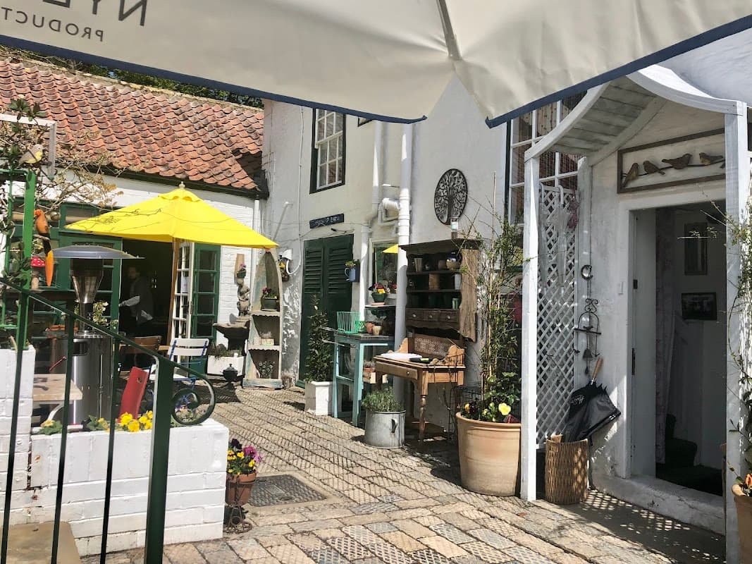 Quaint bar entrance with a sunny courtyard, yellow umbrellas, potted plants, and rustic decor in Crathorne, North Yorkshire.