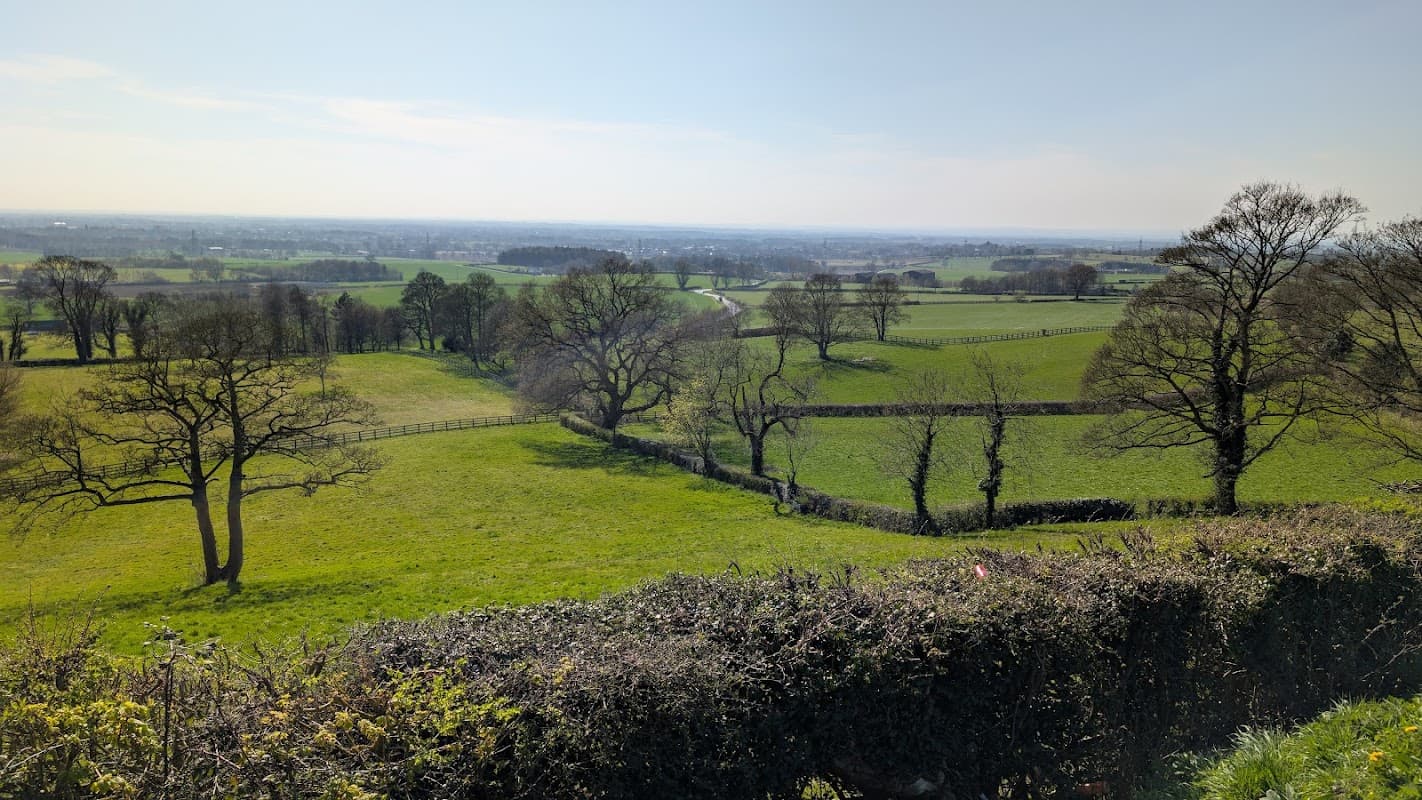 A scenic view from a park bench overlooking lush green fields and distant hills under a clear blue sky.