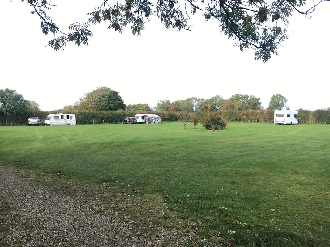 Caravan site with several caravans parked on a lush green lawn, surrounded by trees and hedges in Cropton, Yorkshire.