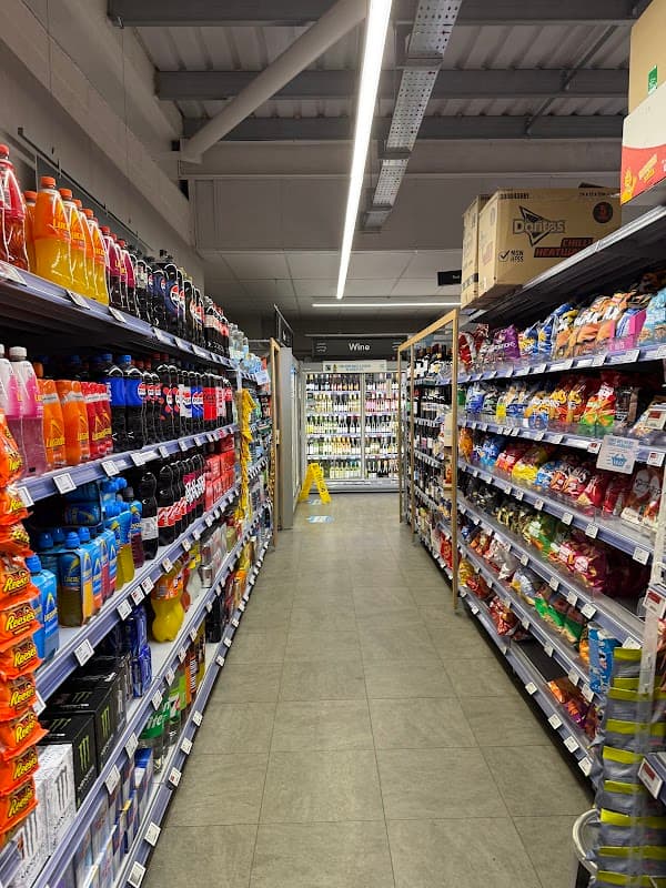 Aisle in a grocery store lined with colorful beverage and snack products, with a caution sign on the floor.
