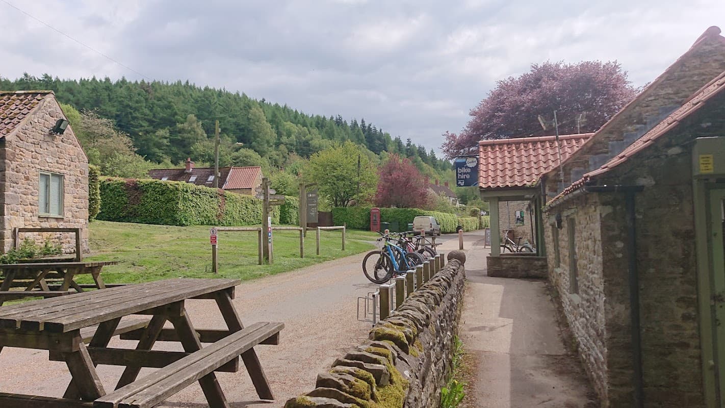 Quaint courtyard with stone buildings, picnic tables, bicycles, and lush greenery in Dalby Forest, Yorkshire.