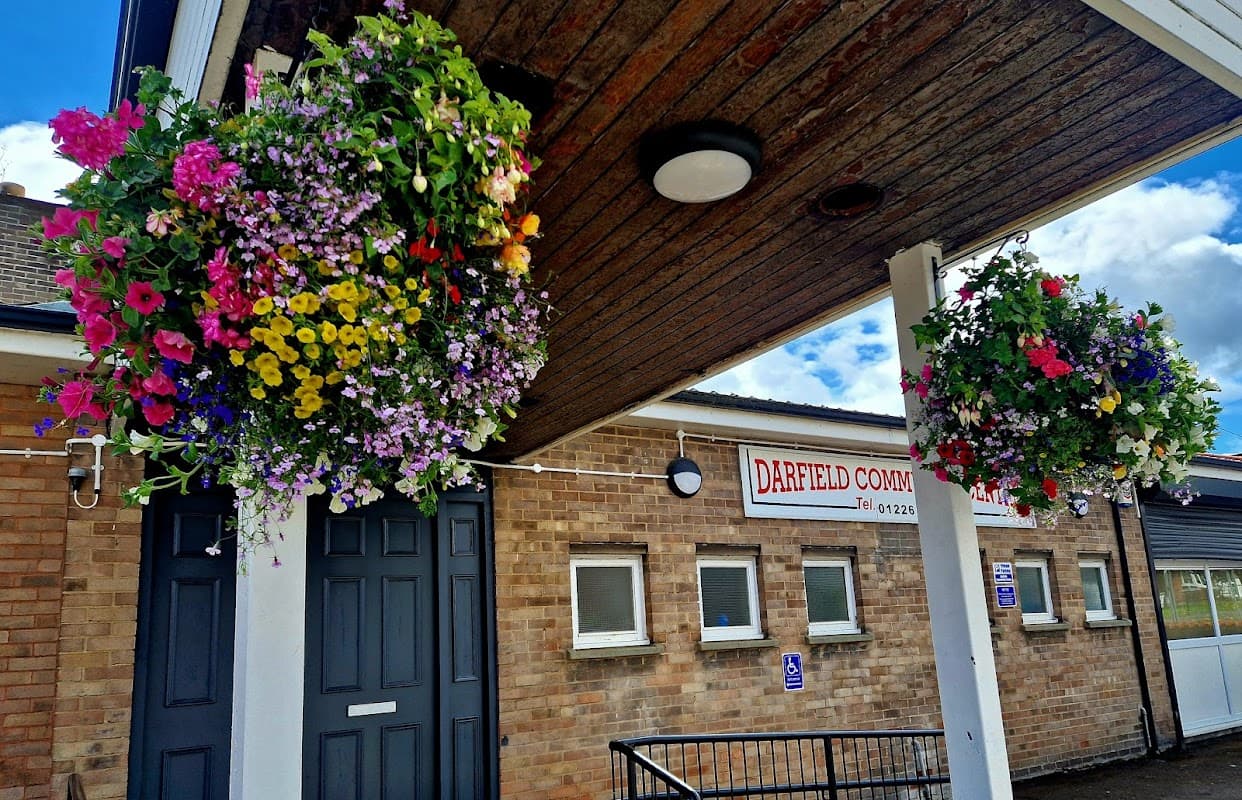 Colorful hanging flower baskets adorn the entrance of Darfield Community Centre, featuring a brick faΓ§ade and signage.