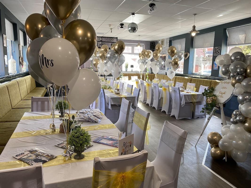 Elegant event setup with white and gold balloons, decorated tables, and chairs in a festive bar setting.