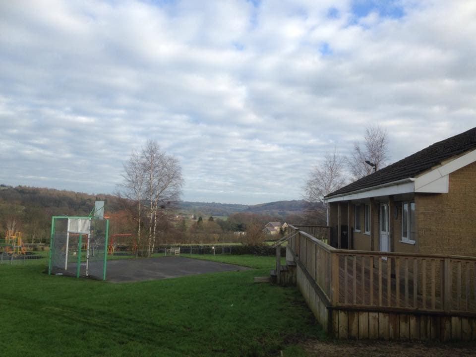 View of Darley Playing Fields with a basketball hoop, grassy area, and rolling hills under a cloudy sky.