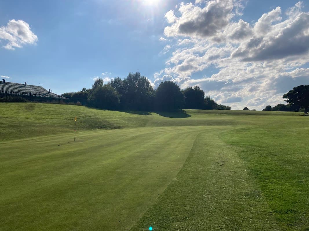 Lush green fairway at Tinsley Park Golf Course under a bright sky with scattered clouds and trees in the background.