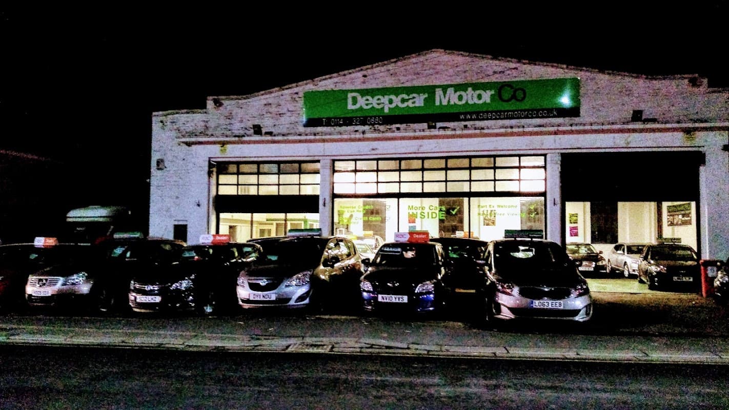 Deepcar Motor Company storefront at night with several cars displayed outside and bright green signage.