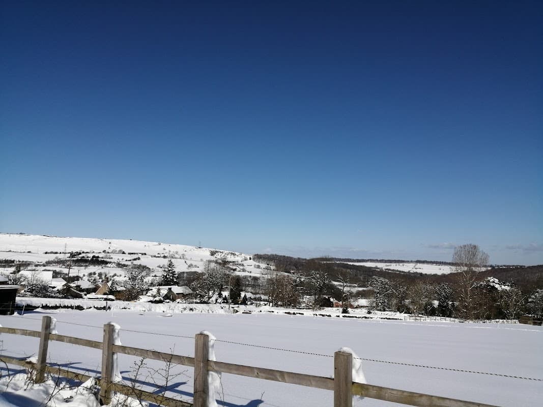 Snow-covered landscape with hills, trees, and a clear blue sky surrounding Deepcar Village Hall.
