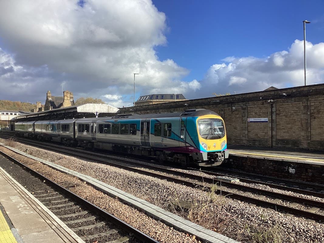 A train at Dewsbury Railway Station, with stone buildings and a blue sky in the background.