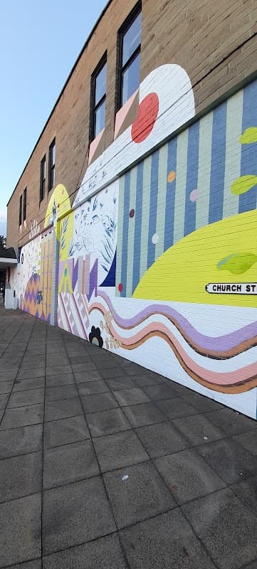 Colorful mural on a building wall, featuring abstract shapes and patterns, with a paved walkway in the foreground.