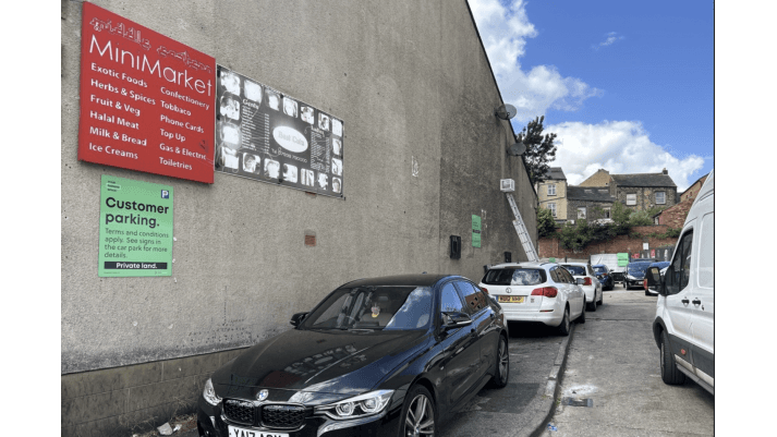 Pay & Display parking area with cars, a MiniMarket sign, and a clear blue sky in Dewsbury, Yorkshire.