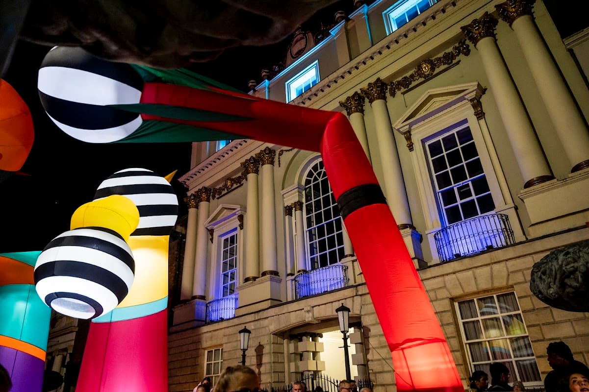 Colorful large balloons and structures in front of a historic building, illuminated at night with vibrant lights.