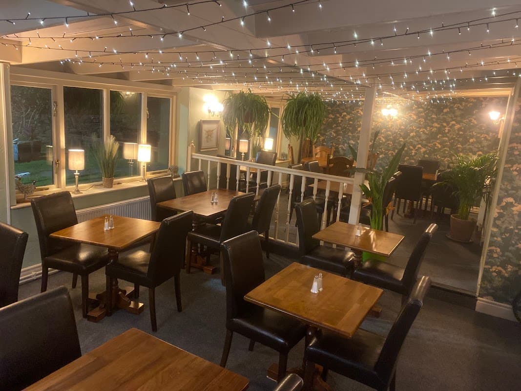 Cozy restaurant interior with wooden tables, black chairs, string lights, and lush plants in Downholme, Yorkshire.