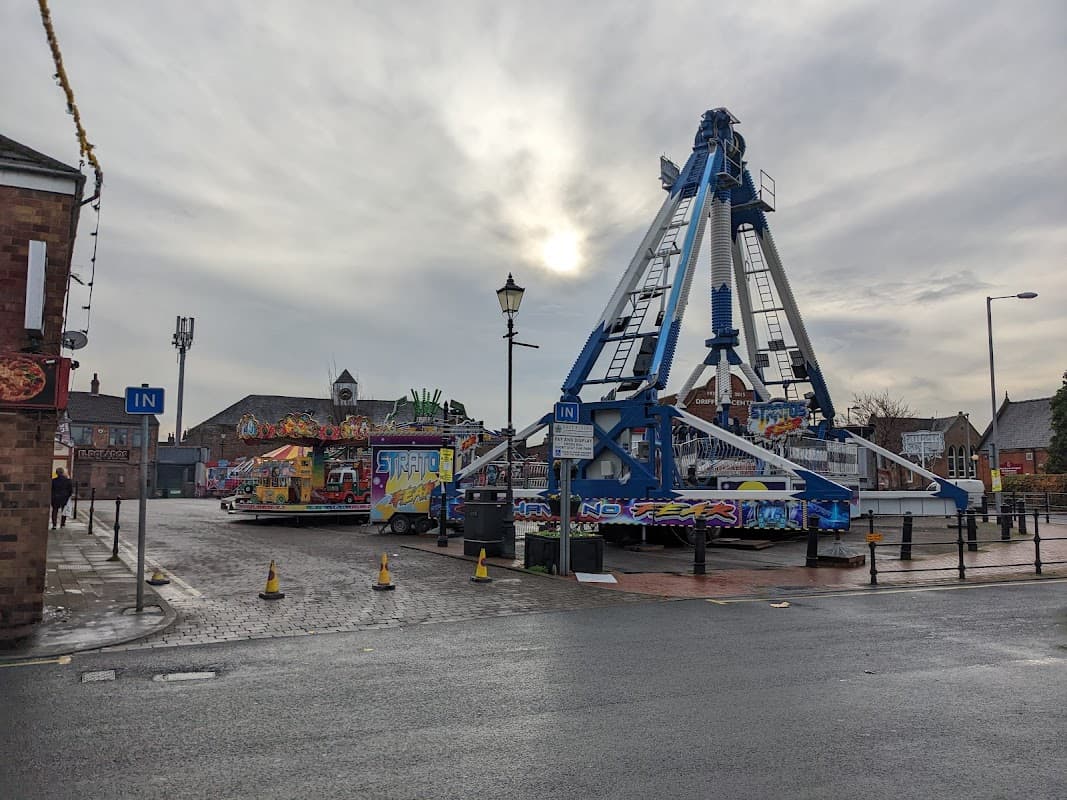 Ferris wheel and colorful fairground rides in a car park, with cloudy sky and street lamps in Driffield, Yorkshire.