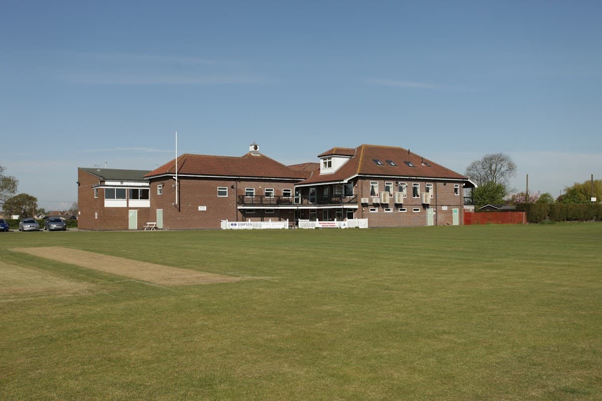 Dunnington & Grimston Sports Club building with cricket pitch in the foreground under a clear blue sky.