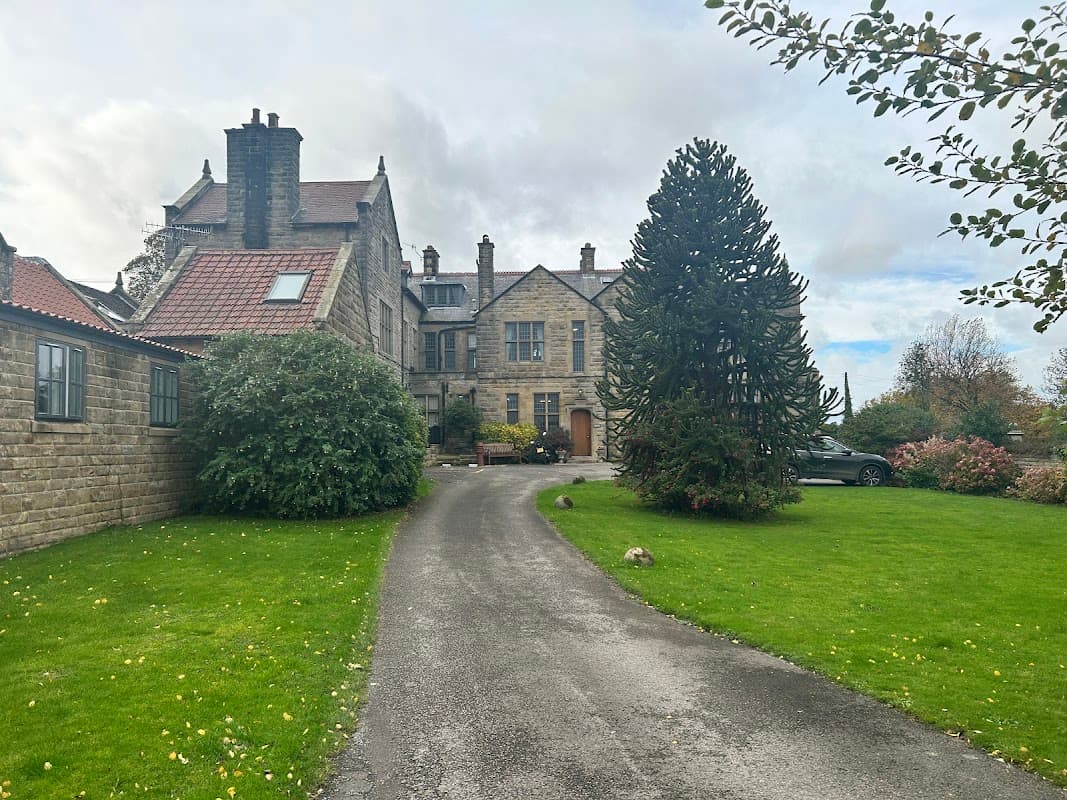 Historic stone building with a landscaped garden and driveway, surrounded by trees and shrubs in Dunsley, North Yorkshire.