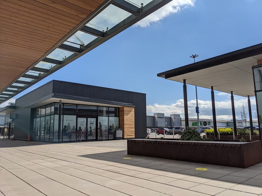 Modern shopping park with glass faΓ§ade, outdoor seating, and clear blue sky in Earswick, Yorkshire.