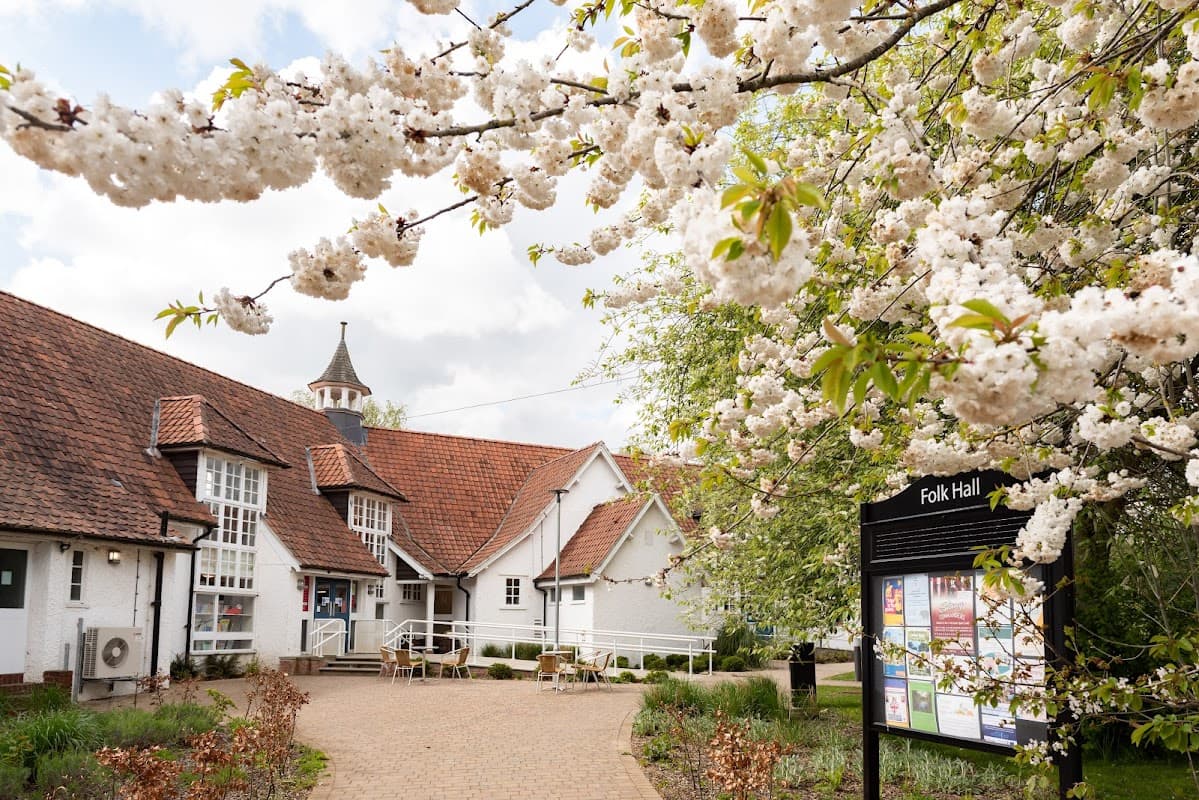 Blossoming cherry trees frame the charming New Earswick Folk Hall, showcasing its distinctive architecture and inviting entrance.