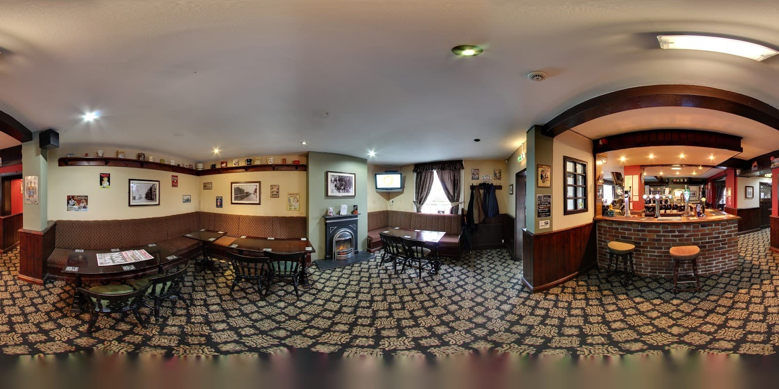 Cozy pub interior with patterned carpet, wooden tables, a bar area, and vintage decor on the walls.