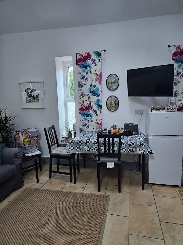 Cozy interior of East Cowton Village Hall featuring a dining table, chairs, fridge, and floral decor.