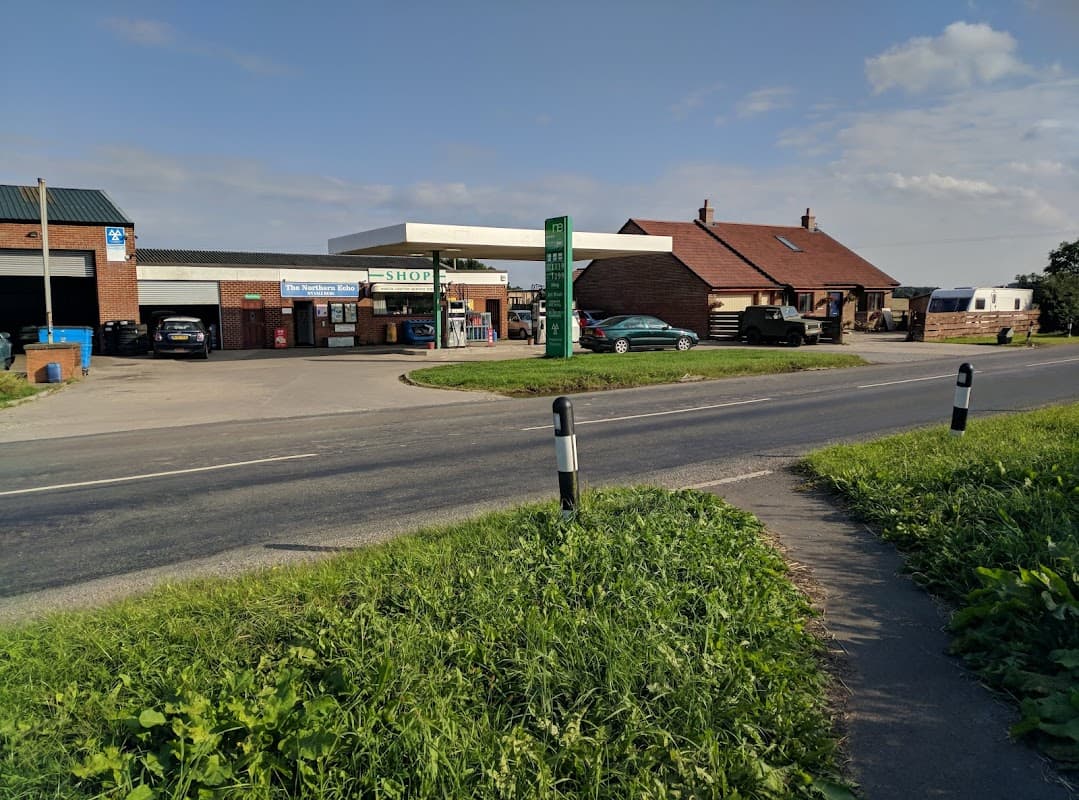 North Cowton Service Station with a shop, fuel pumps, and parked vehicles along a rural road in Yorkshire.