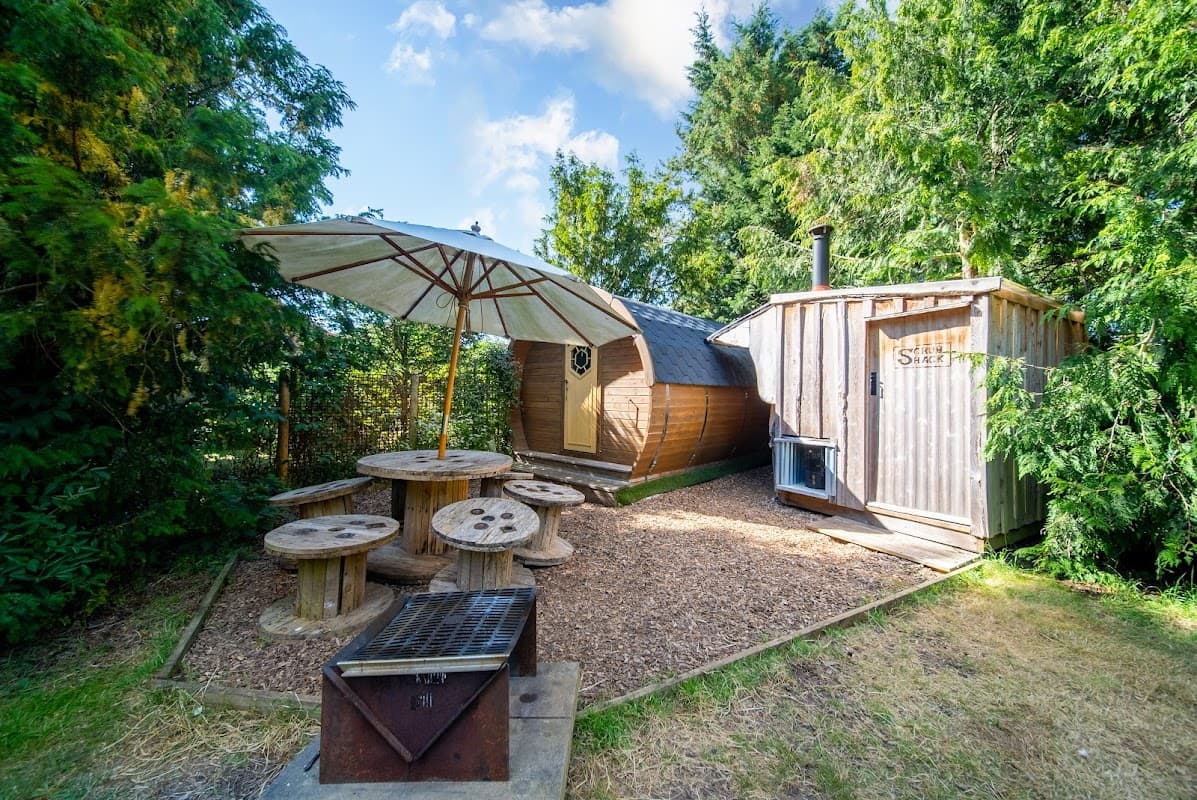 Wooden glamping cabin with an umbrella, picnic table, and outdoor grill surrounded by greenery in East Heslerton, Yorkshire.