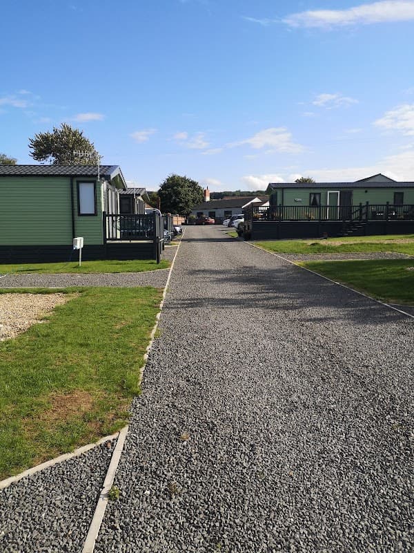 Gravel pathway lined with green lodges, leading to a bright blue sky in East Heslerton, Yorkshire.