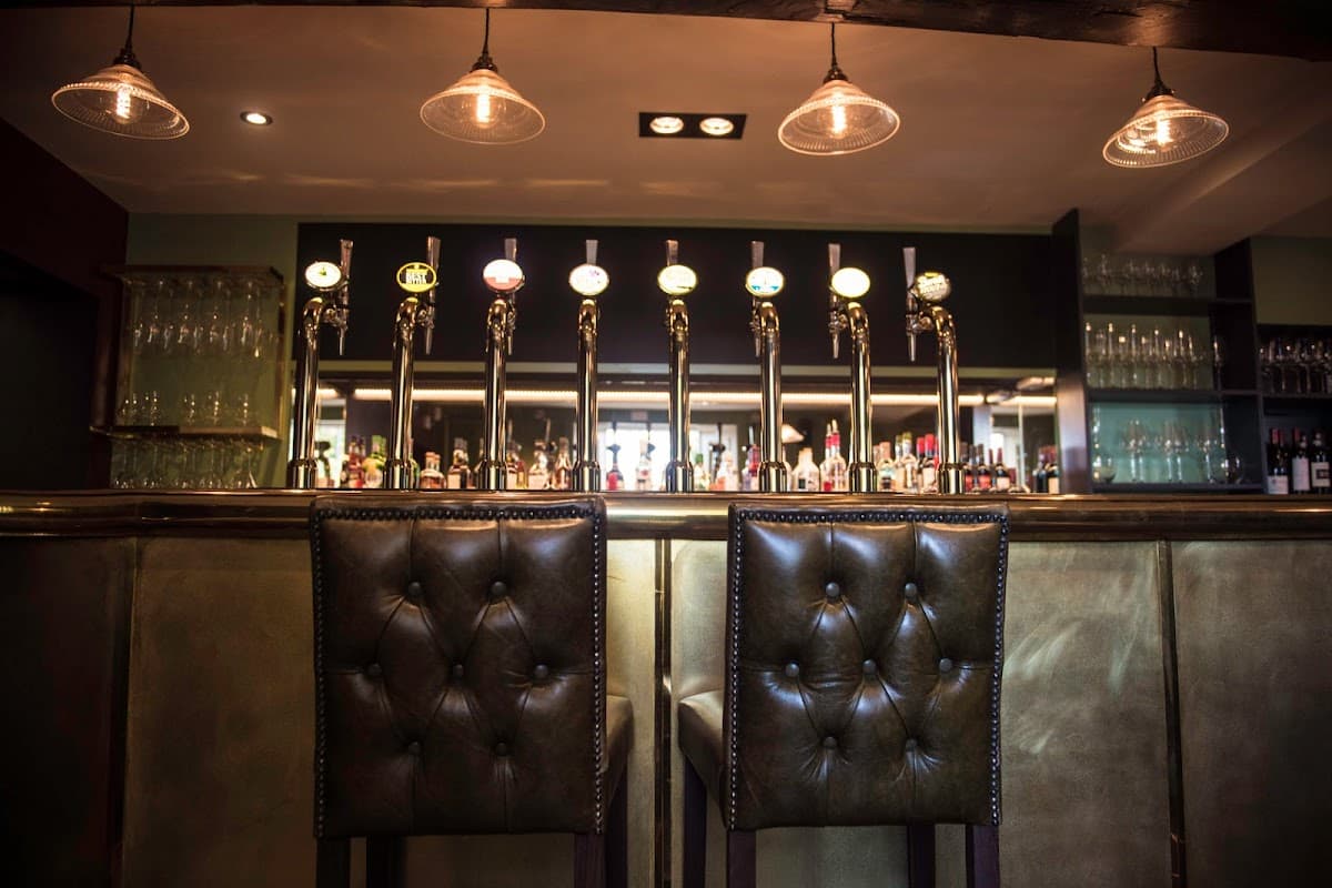 Elegant bar area with polished taps, glassware, and stylish leather stools under warm pendant lighting.