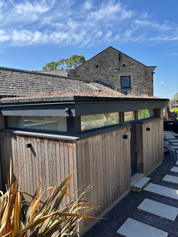 Modern wooden structure with a green roof, surrounded by stone buildings and a landscaped garden in East Marton, Yorkshire.