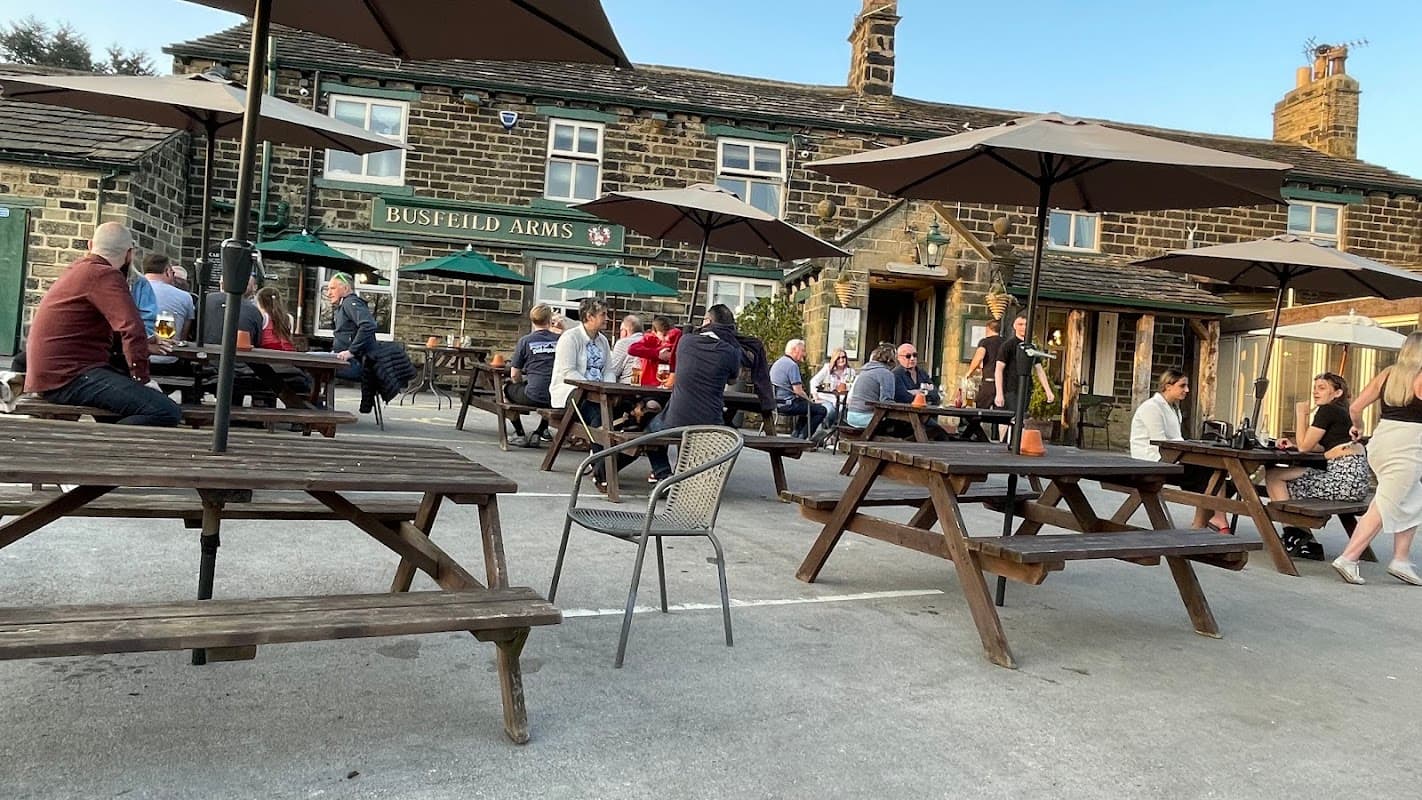 Outdoor seating area with wooden tables, umbrellas, and patrons enjoying drinks at Busfeild Arms in East Morton.