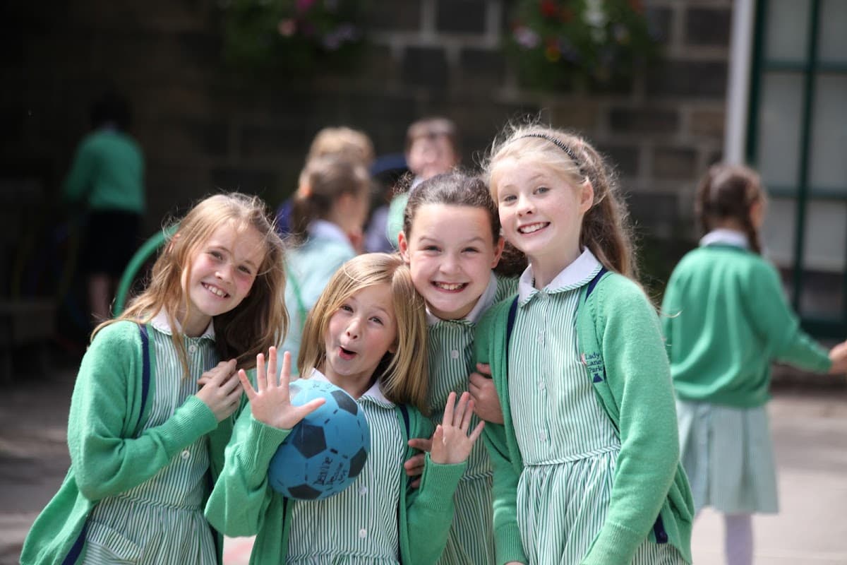 Four smiling girls in green cardigans and striped dresses, holding a blue ball, enjoying time at Lady Lane Park School.