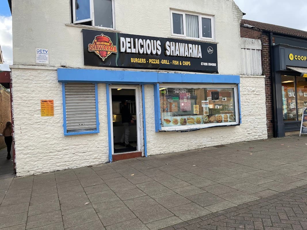 Restaurant exterior with a sign reading "Delicious Shawarma," featuring a menu display and nearby shops in Eastfield.