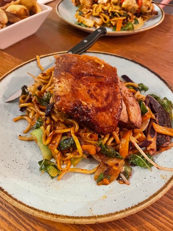 A plate of crispy pork on stir-fried noodles with vegetables, served at Black Swan bar in Eastrington, Yorkshire.