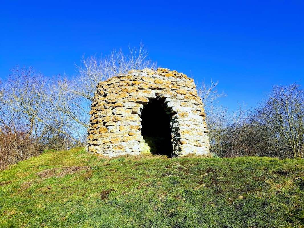 Stone structure atop a grassy mound, surrounded by bare trees under a clear blue sky.