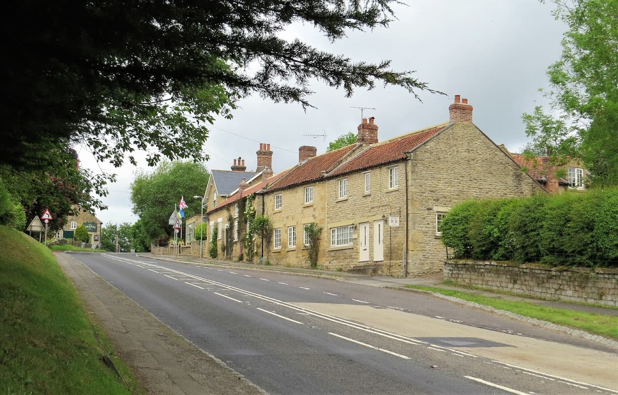 Chestnut Holiday Cottage, a stone building with a red-tiled roof, along a quiet road lined with greenery in Ebberston.