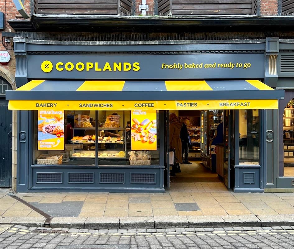 Cooplands bakery storefront with yellow awning, displaying pastries, sandwiches, and coffee options.