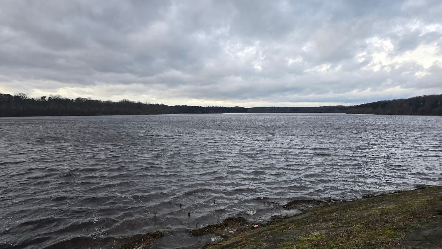 Expansive Eccup Reservoir under a cloudy sky, with rippling water and a tree-lined shoreline.