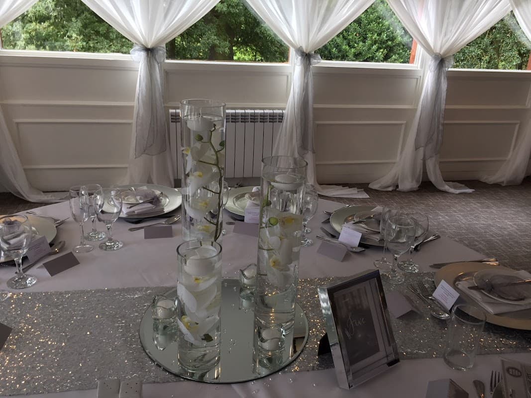 Elegant table setting with glass vases, white flowers, and silver accents, surrounded by sheer drapery.