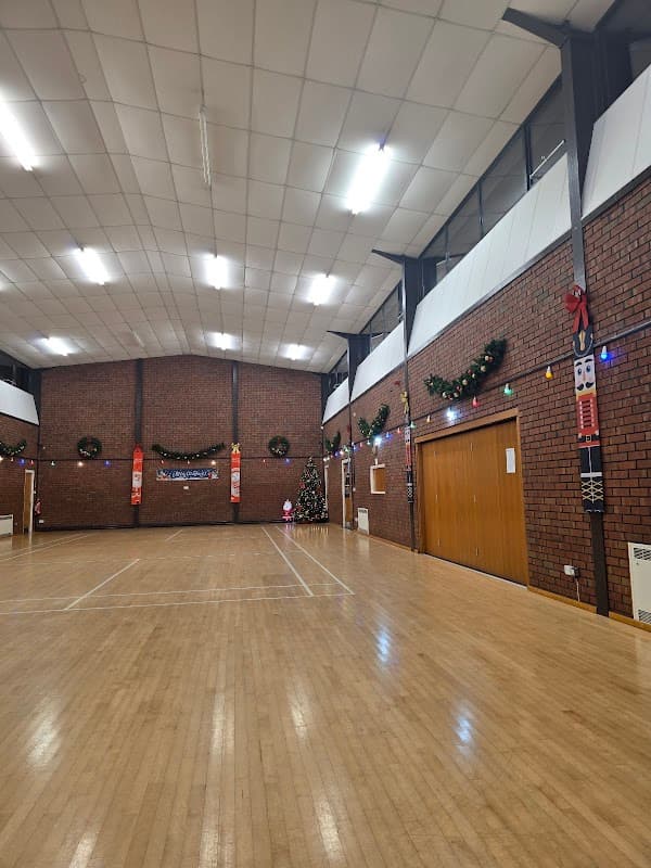 Spacious event venue with wooden flooring, decorated walls, and festive lights, featuring a Christmas tree in the corner.