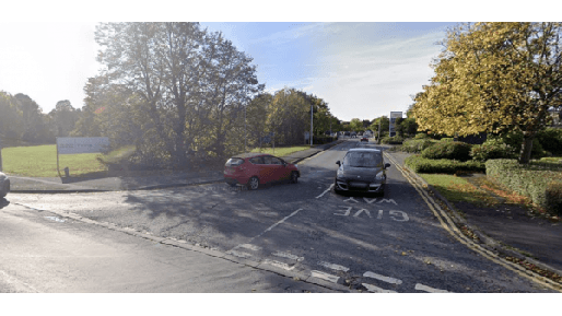 Car park entrance in Edenthorpe, Yorkshire, with trees and parked cars along a winding road.
