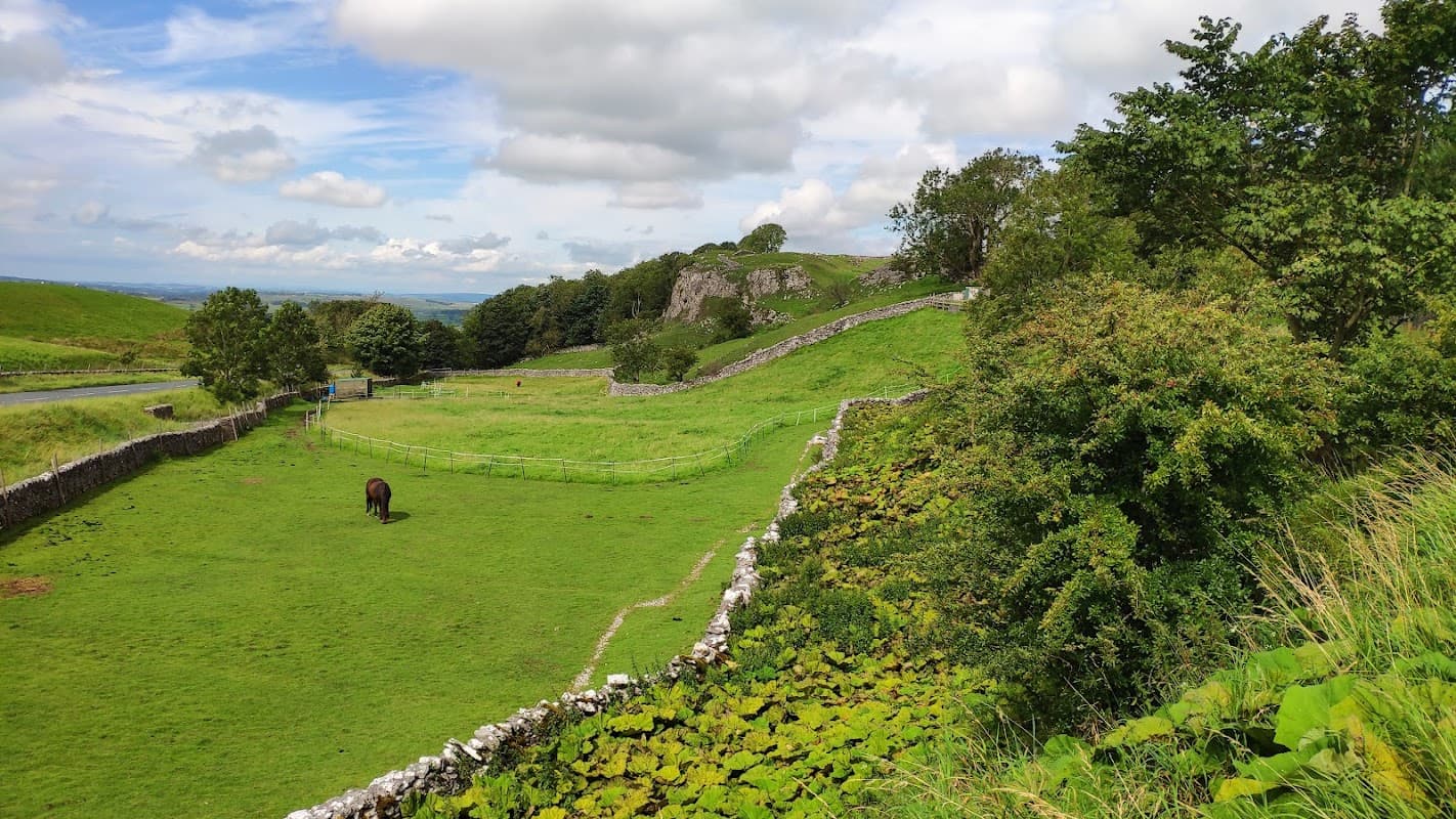 Lush green fields with a horse grazing, stone walls, and rolling hills under a partly cloudy sky in Eldroth, Yorkshire.