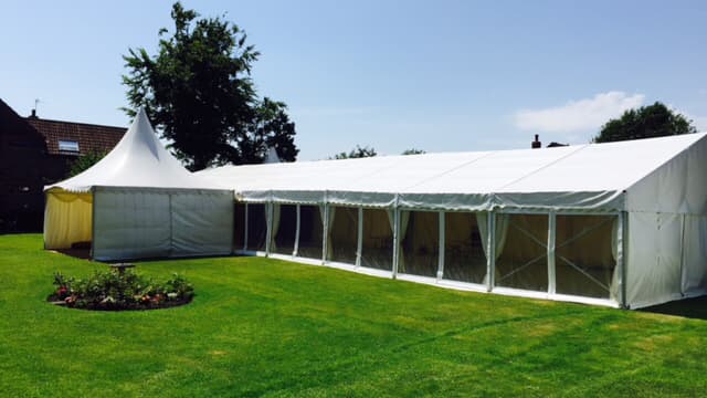 Large white marquee with clear sides set on a green lawn, surrounded by trees and a garden in Escrick, Yorkshire.